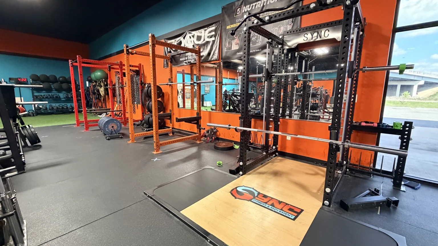 Squat racks and a Sync-branded lifting platform beside the turf area