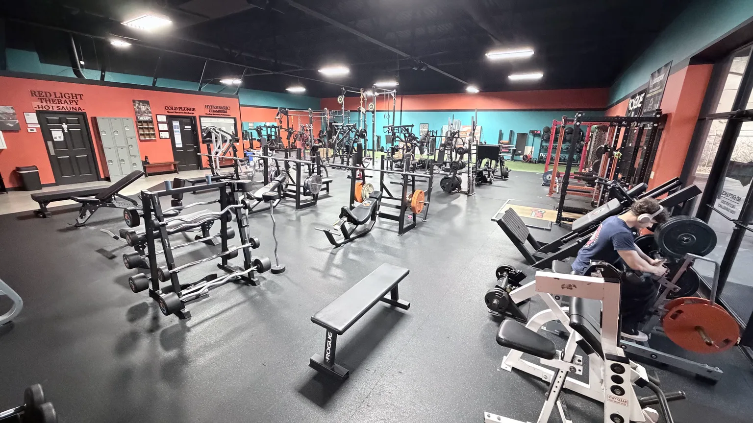 Wide view of Sync’s strength machines, benches and free weights, with turf in the background